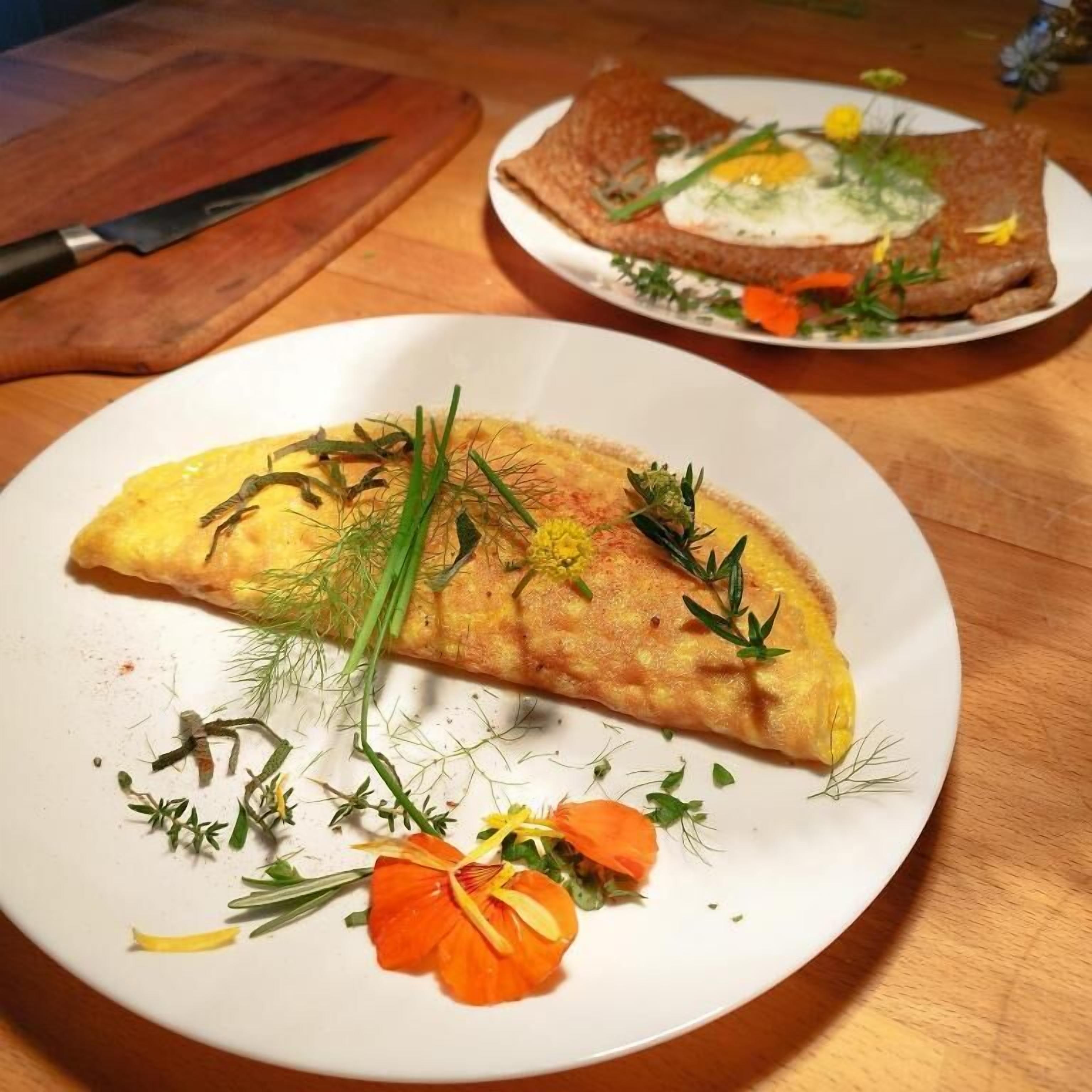 A plate of food with an omelette, garnished with herbs and flowers.