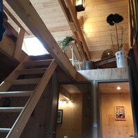 Un interior de madera con zona de entrepiso, una escalera y una puerta que da a otra habitación.