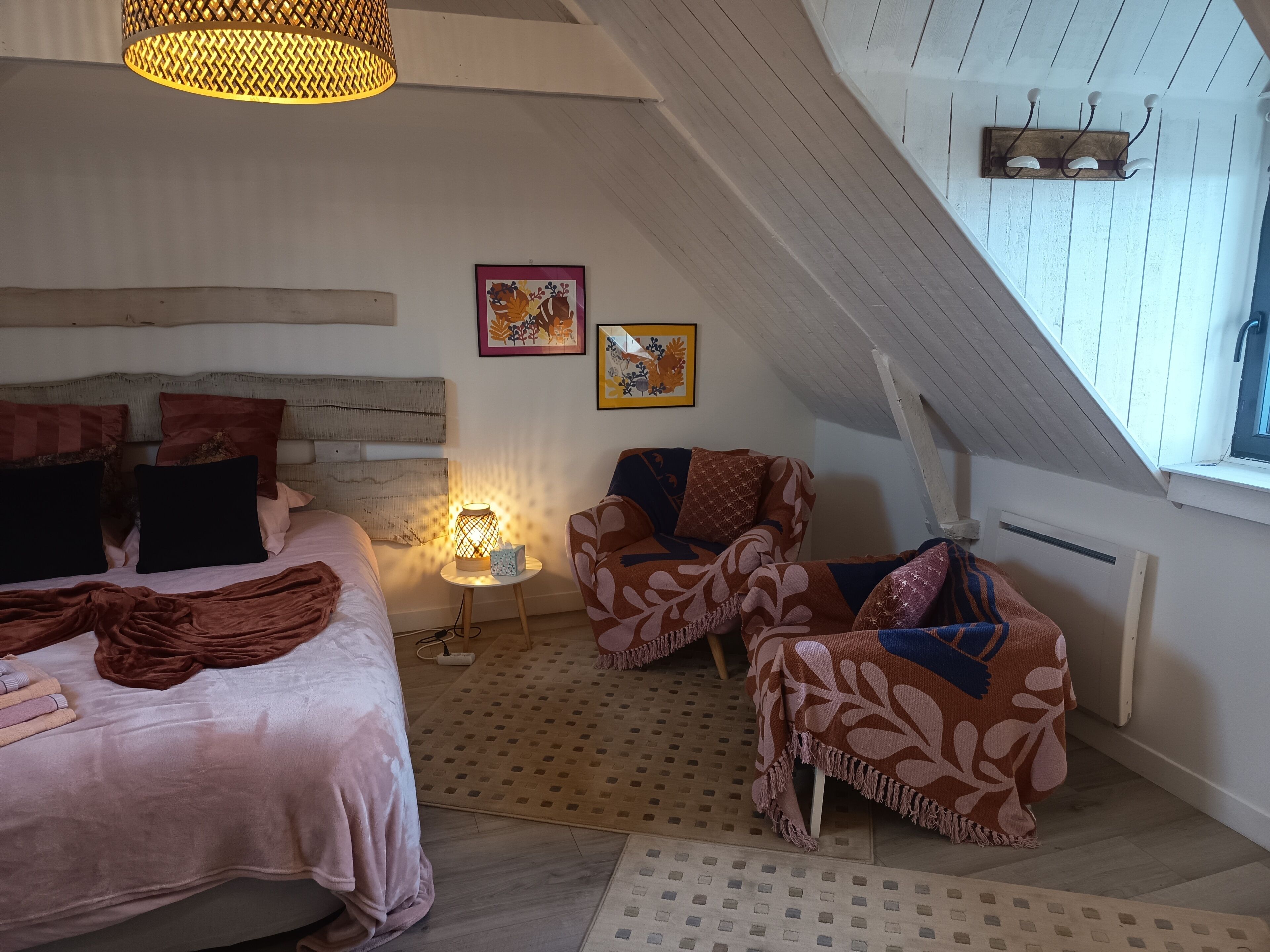 A bedroom with a bed, two chairs, a table with a lamp, and artwork on the wall.
