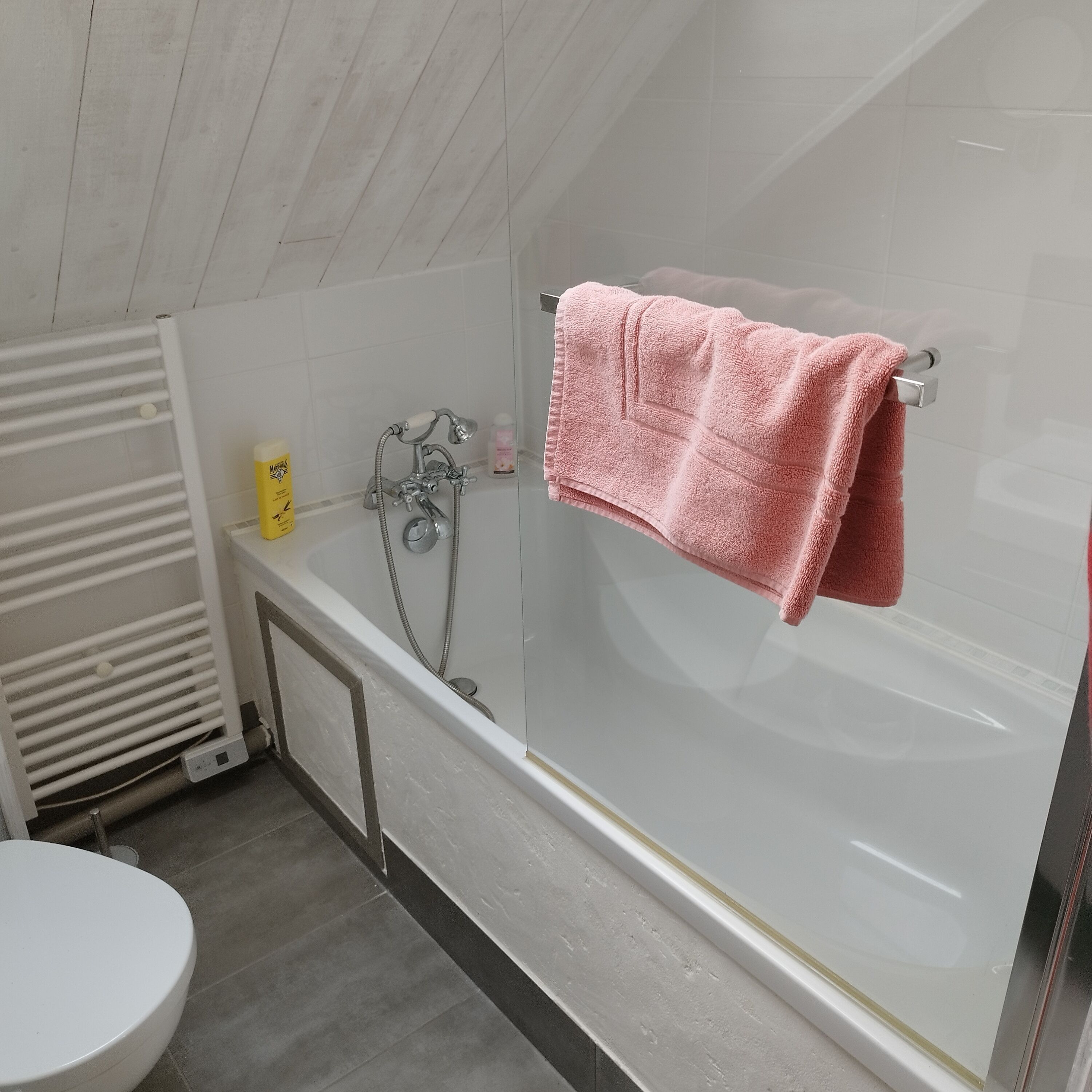 Un bagno moderno con cabina doccia in vetro, un water bianco e un porta asciugamani con un asciugamano rosa.