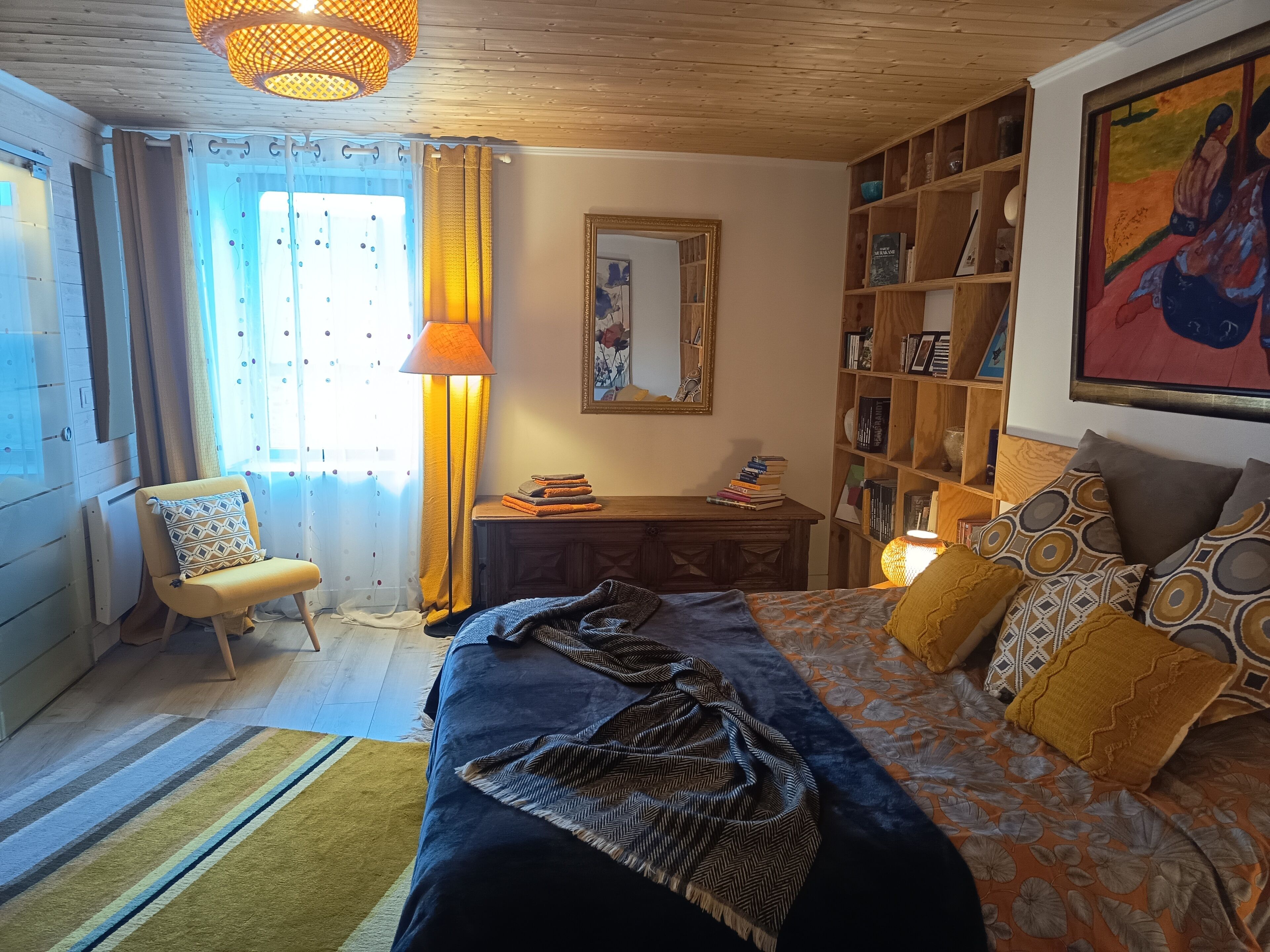 A bedroom with a bed, a chair, a desk, a bookshelf, and a window with curtains.