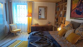 A bedroom with a bed, a chair, a desk, a bookshelf, and a window with curtains.