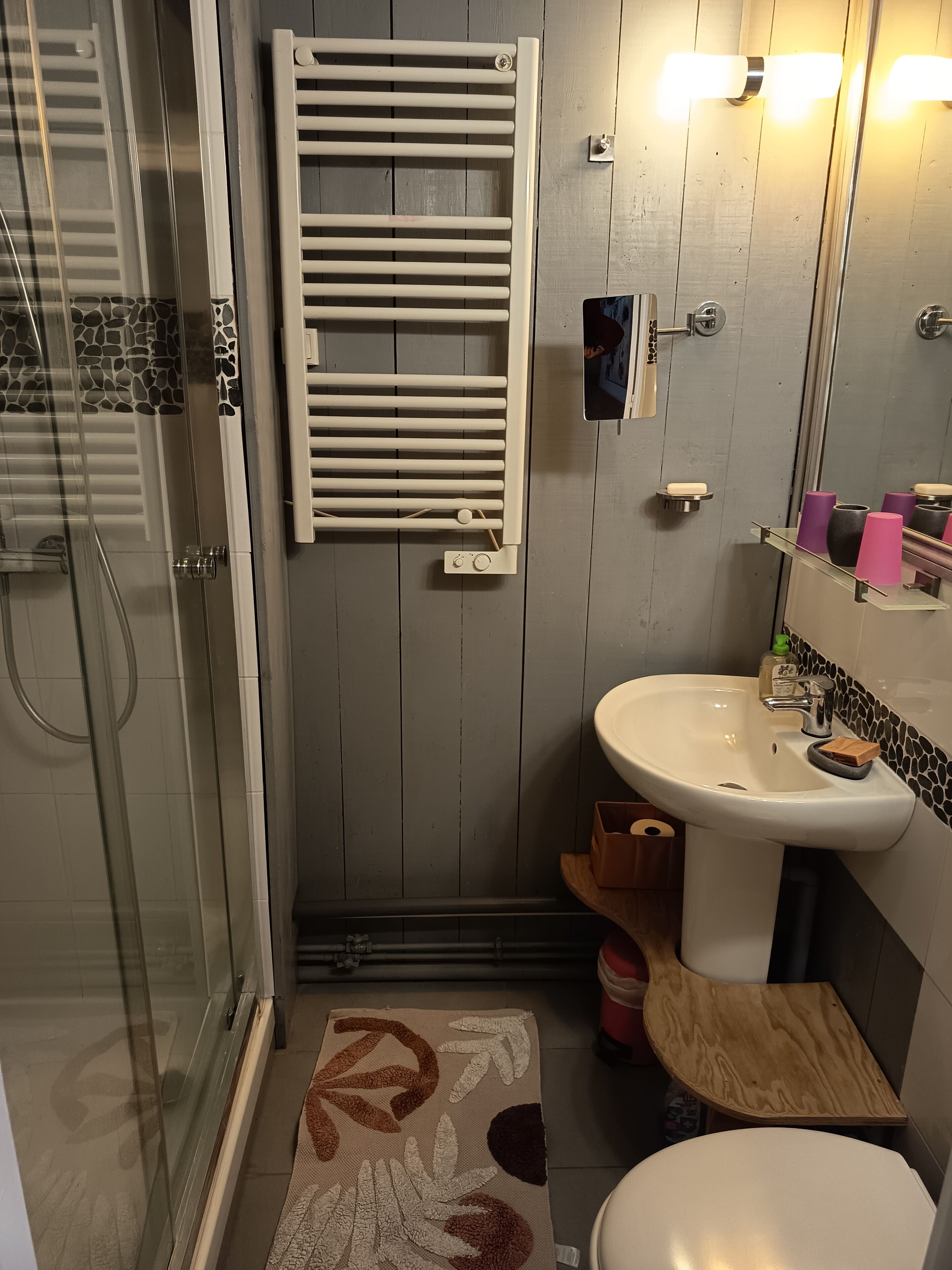Ein Badezimmer mit Duschkabine aus Glas, einem weißen Waschbecken mit Seifenschale und einem Handtuchhalter.