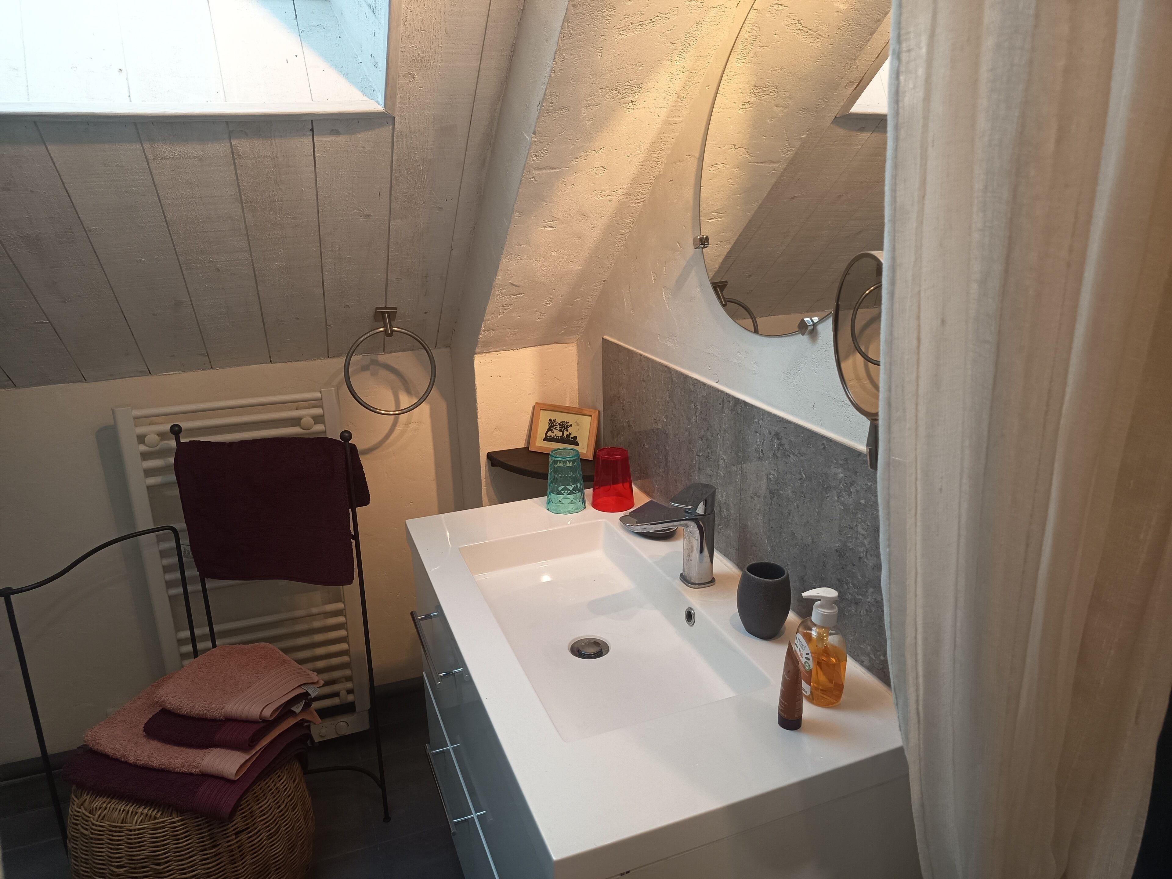 Een badkamer met een wit wastafel, een handdoekrek met handdoeken, een klein plankje met toiletartikelen en een spiegel.