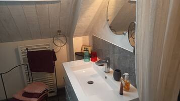 Een badkamer met een wit wastafel, een handdoekrek met handdoeken, een klein plankje met toiletartikelen en een spiegel.