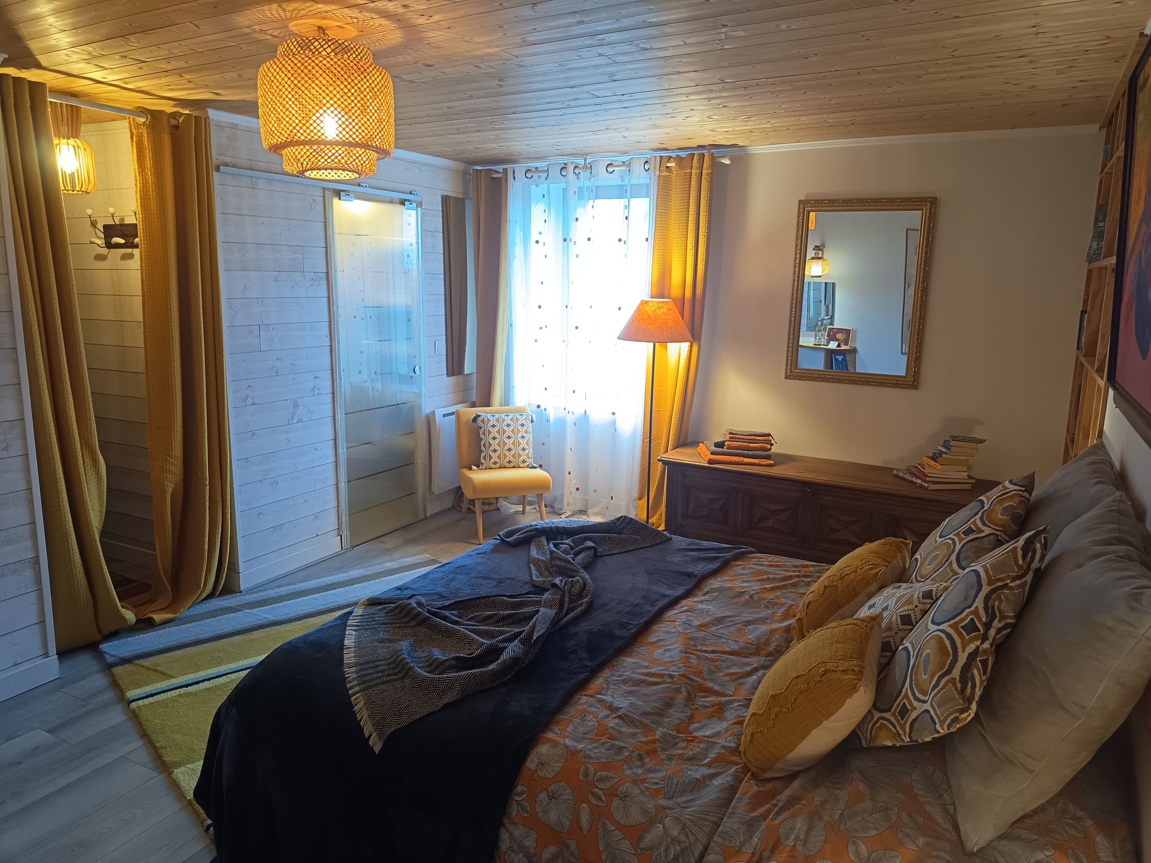 A bedroom with a bed, a chair, a dresser, a mirror, and a window with curtains.
