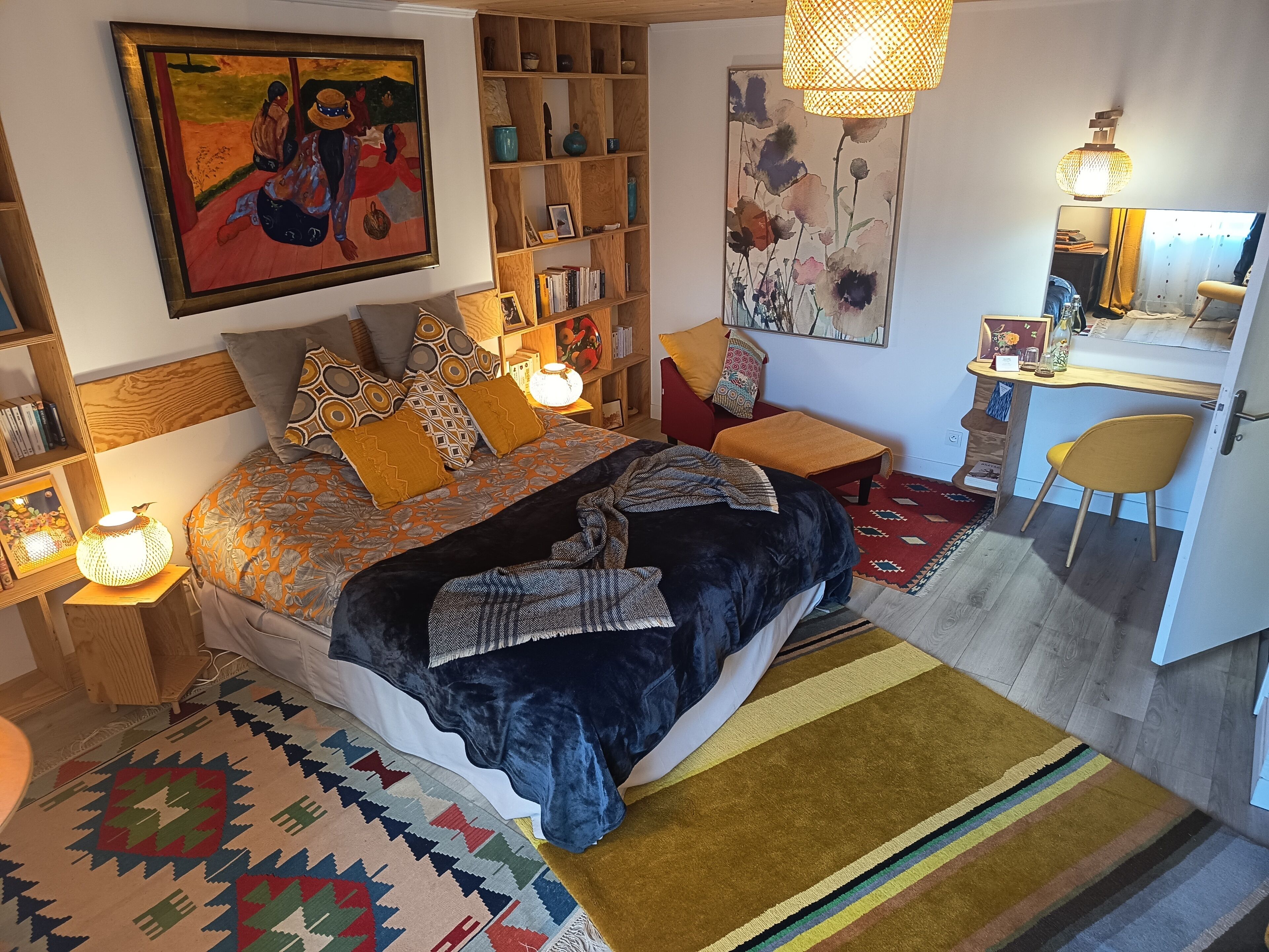 A bedroom with a bed, bedside tables, a desk, a chair, a bookshelf, and a painting on the wall.