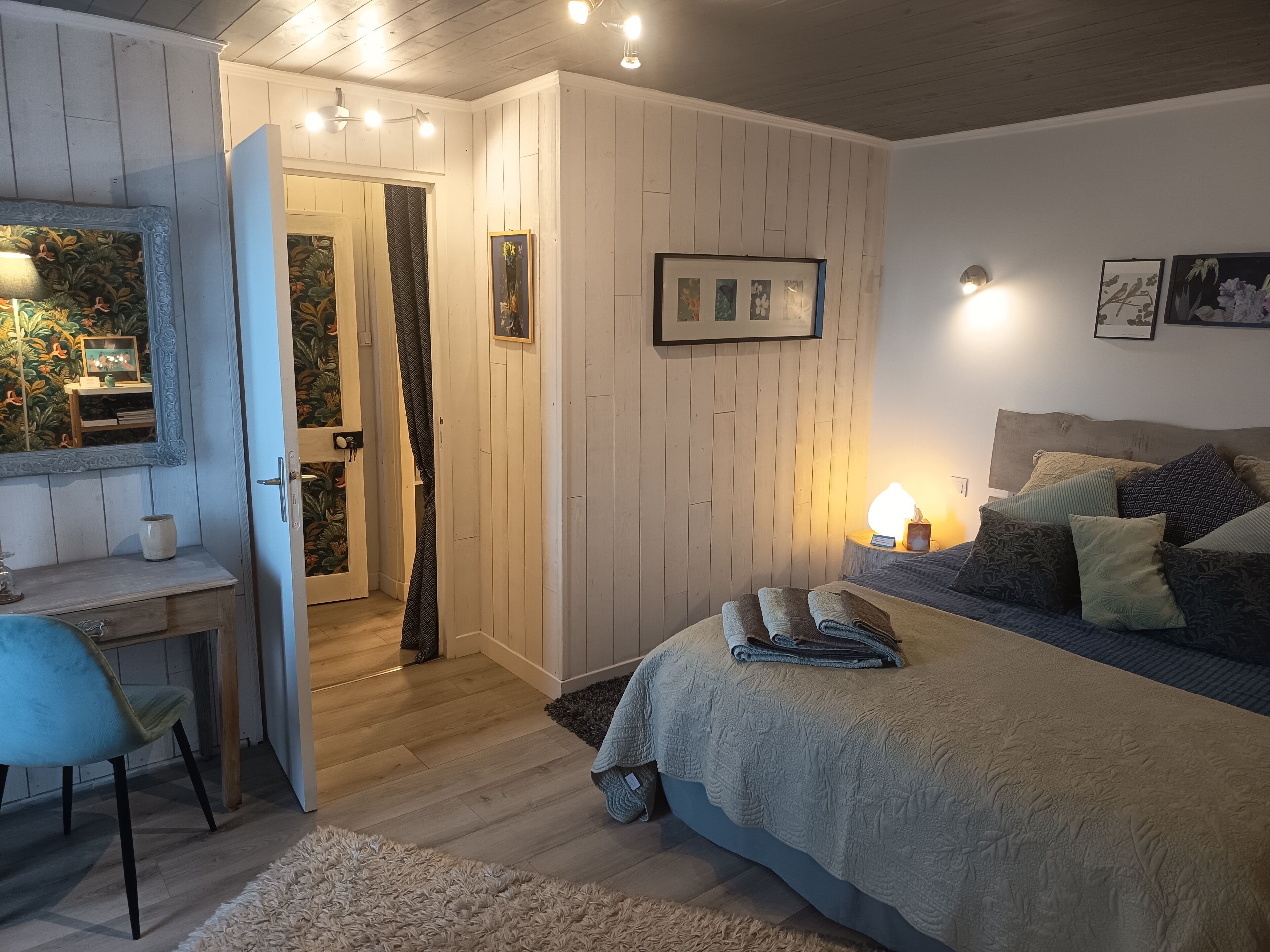 Un dormitorio con cama, mesita de noche, lámpara y una puerta que da a otra habitación.