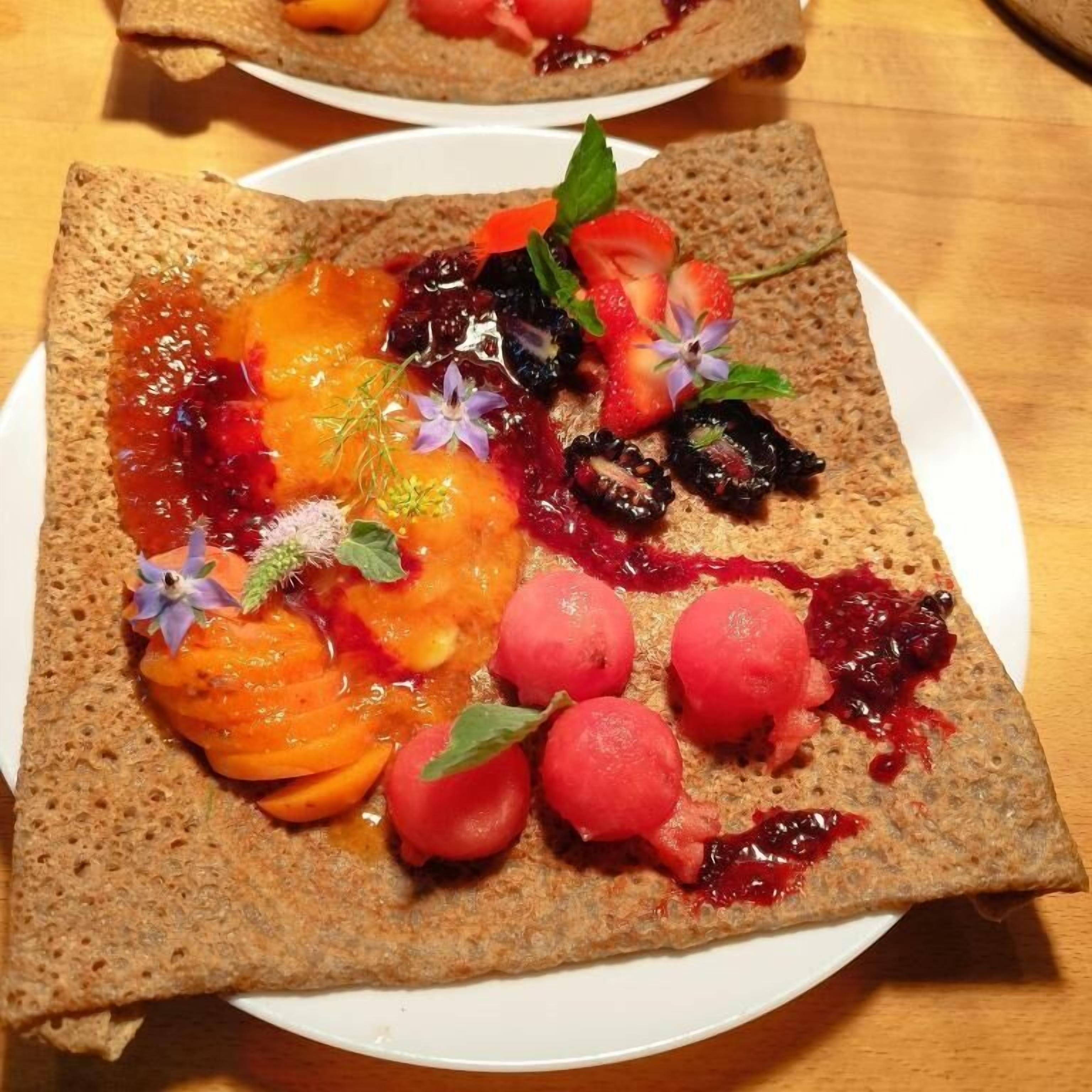 A plate with a crepe topped with fruit and berries.