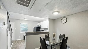 A modern kitchen with a central island, a dining area with a glass table and black chairs, and a clock on the wall.