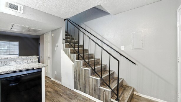 A kitchen with a dishwasher, a staircase with wooden steps and black railings, and a white ceiling with an air vent.