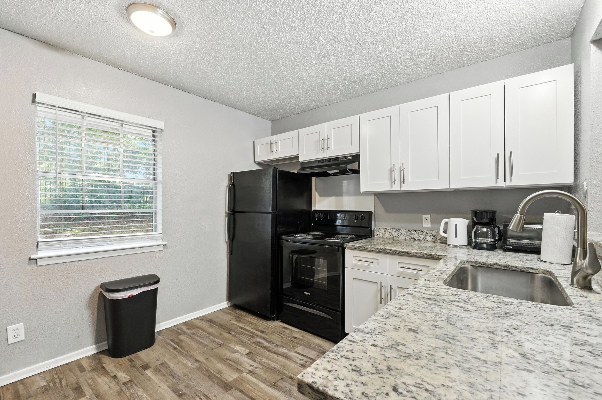 A compact kitchen with white cabinets, a black refrigerator, a stove, and a sink.