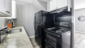 A compact kitchen with a black refrigerator, stove, and oven, white cabinets, and a granite countertop.