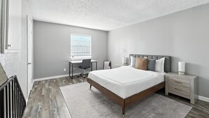 A bedroom with a bed, bedside tables, a desk, and a window.
