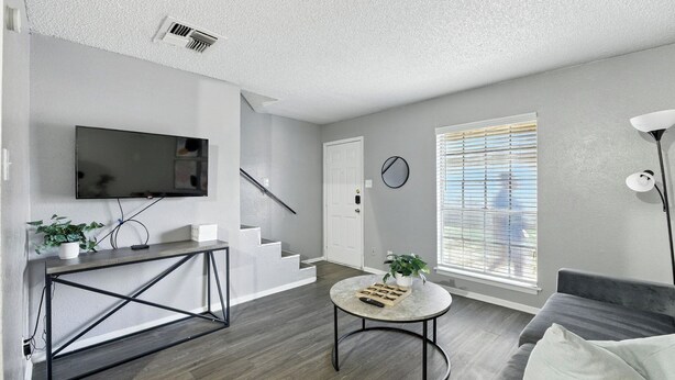 A modern living room with a TV, a staircase, a round coffee table, and a gray sofa.