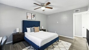 A bedroom with a bed, nightstands, a ceiling fan, and a door.
