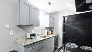 A compact kitchen with gray cabinets, a black refrigerator, a microwave, and a sink.