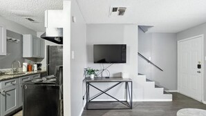 A modern kitchen with stainless steel appliances, a dining area with a TV, and a staircase leading to another level.