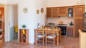 A compact kitchen with wooden cabinets, a dining table with chairs, and a small island with a sink. - Stunning private villa for 4 people with WIFI, A/C, TV, patio, pets allowed and panoramic view (Olbia)