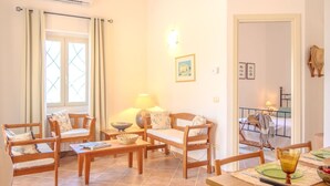 A cozy living room with a sofa, chairs, a dining table, and a lamp. - Stunning private villa for 4 people with WIFI, A/C, TV, patio, pets allowed and panoramic view (Olbia)