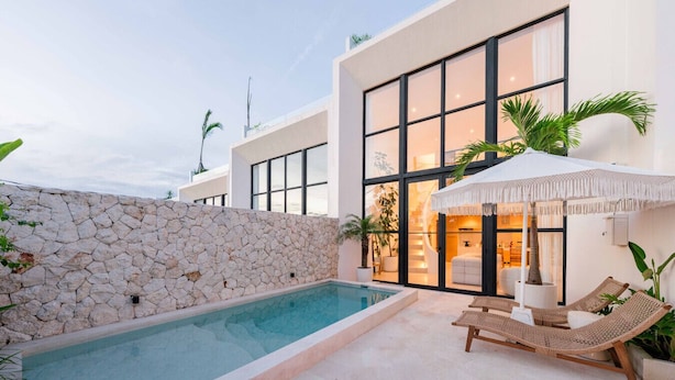 Une maison moderne dotée d’une piscine, d’un mur en pierre et d’un espace extérieur aménagé avec des parasols.