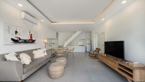 Una sala de estar moderna con un sofá gris, otomanas de mimbre, un mueble de televisión de madera y un televisor de pantalla plana.