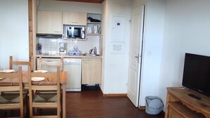 A compact kitchen with a microwave, coffee maker, and dishwasher. There is a dining area with wooden chairs and a table, and a television on a wooden stand. - Spacious apartment in Super-Besse with terrace and garage (Besse-et-Saint-Anastaise-Super Besse)