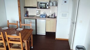 A compact kitchen with a dining table and chairs, a microwave, a toaster, and a refrigerator. - Spacious apartment in Super-Besse with terrace and garage (Besse-et-Saint-Anastaise-Super Besse)