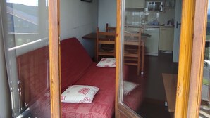 A compact living space with a red sofa, a wooden chair, and a small kitchen area visible through an open door. - Spacious apartment in Super-Besse with terrace and garage (Besse-et-Saint-Anastaise-Super Besse)