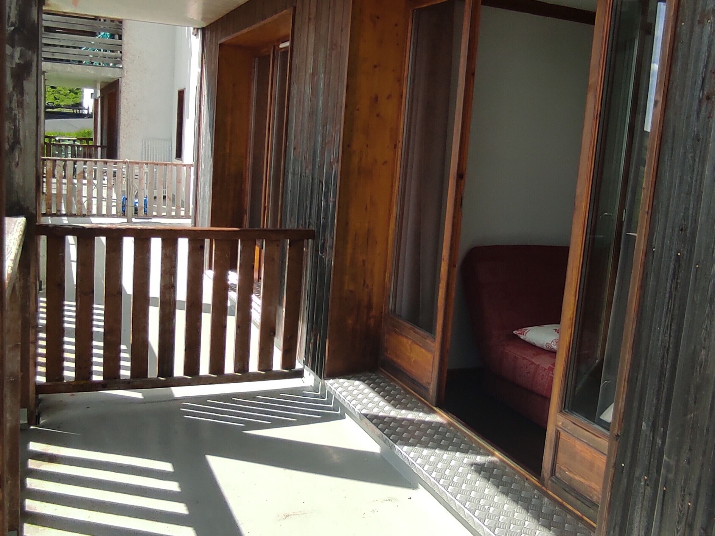 Un balcon en bois avec une rambarde en m étal, un canapé rouge et une vue sur l’extérieur.