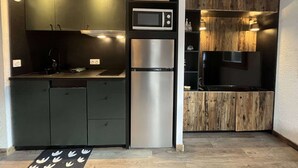 Una cocina compacta con microondas integrado, refrigerador de acero inoxidable y muebles de madera.