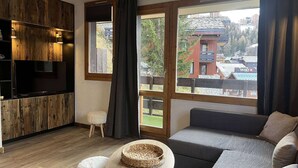 Una habitación moderna con una pared de acento de madera, un sofá gris, una pequeña mesa redonda y vistas a un edificio con un telesilla.
