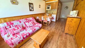 A cozy room with a wooden sofa, a wooden table, a kitchen area with wooden cabinets, and a small refrigerator. - Studio for 4 at 3 Valleys Ski-in/Ski-out (Les Menuires)