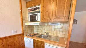A compact kitchen with wooden cabinets, a microwave, a sink, and a dishwasher. - Studio for 4 at 3 Valleys Ski-in/Ski-out (Les Menuires)