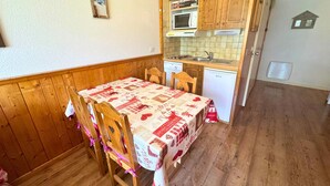 A dining area with a wooden table and chairs, a kitchen with wooden cabinets and a microwave, and a small window. - Studio for 4 at 3 Valleys Ski-in/Ski-out (Les Menuires)