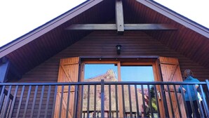 Una cabaña de madera con balcón, un ventanal grande y vistas a la montaña.