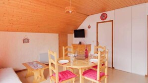 Una habitación acogedora con techo de madera, una mesa de comedor con sillas, un televisor en la pared y una puerta.