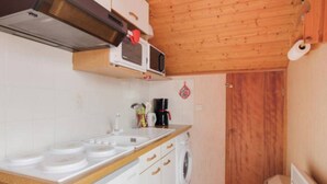 Cocina compacta con armarios blancos, microondas, cafetera y techo de madera.