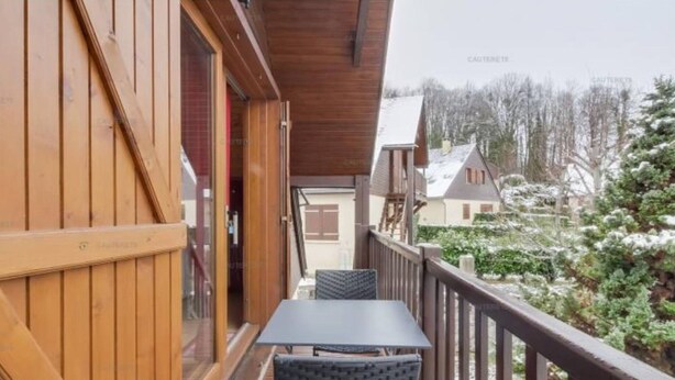 Un balcón de madera con una mesa y sillas, con vistas a un paisaje nevado y edificios.
