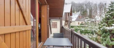 A wooden balcony with a table and chairs, overlooking a snowy landscape and buildings.
