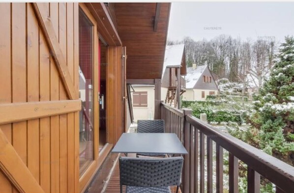 Un balcón de madera con una mesa y sillas, con vistas a un paisaje nevado y edificios.
