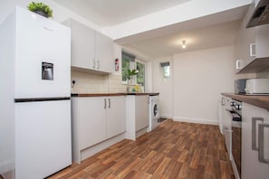A modern kitchen with white cabinetry, a built-in washing machine, and a wooden floor. - Vacant Nests | The Darwin | Stylish | Wifi (Hartlepool)
