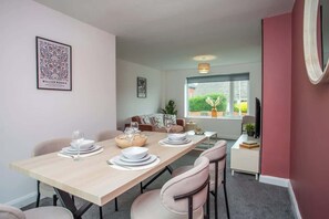 A dining area with a table set for four, a sofa, and a window with a view of greenery. - Vacant Nests | The Darwin | Stylish | Wifi (Hartlepool)