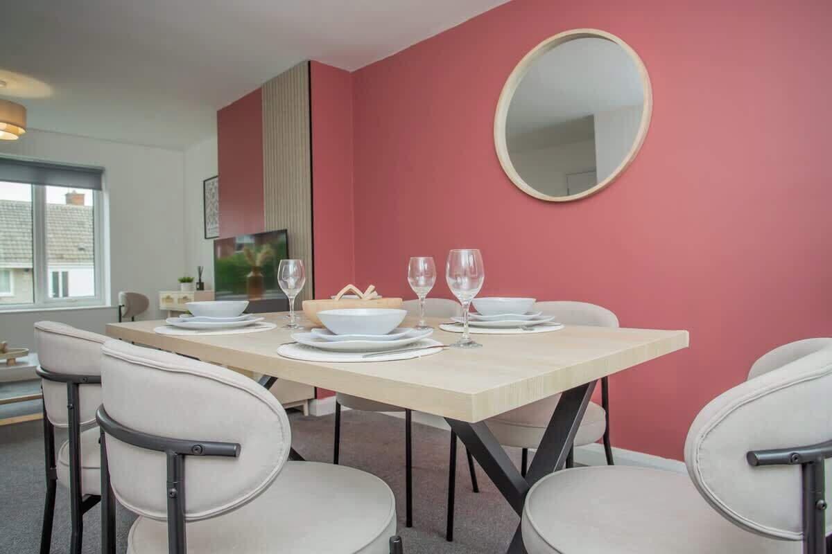 A dining area with a table set for four, chairs, a round mirror, and a red accent wall.