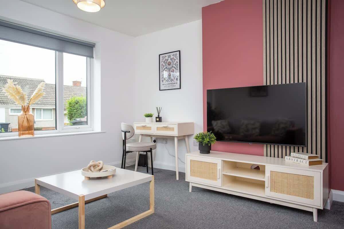 Ein modernes Wohnzimmer mit großem Fernseher, einem weißen Schreibtisch, einem Sessel und einer Couch.