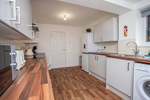 A compact kitchen with white cabinets, a wooden countertop, a built-in washing machine, and a window above the sink.