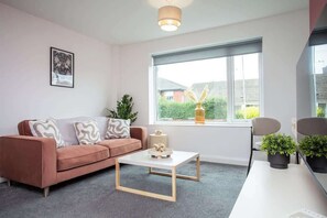 A modern living room with a sofa, coffee table, and chairs, a window with a view, and a framed picture on the wall. - Vacant Nests | The Darwin | Stylish | Wifi (Hartlepool)