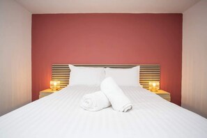 A neatly made bed with white linens, two bedside lamps, and a red accent wall. - Vacant Nests | The Darwin | Stylish | Wifi (Hartlepool)