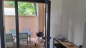 An open sliding glass door leading to an outdoor patio area with a barbecue grill, a table, and chairs. - Barn La Roca Masia - Les Pivoines, swimming pool, garden, 1 bedroom 2/4 persons (Assier)