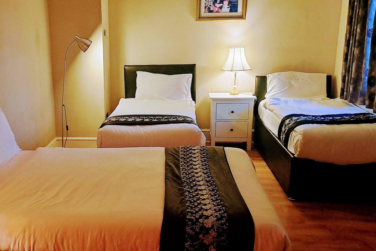 A hotel room with two beds, a nightstand with a lamp, a bedside table, and a framed picture on the wall.